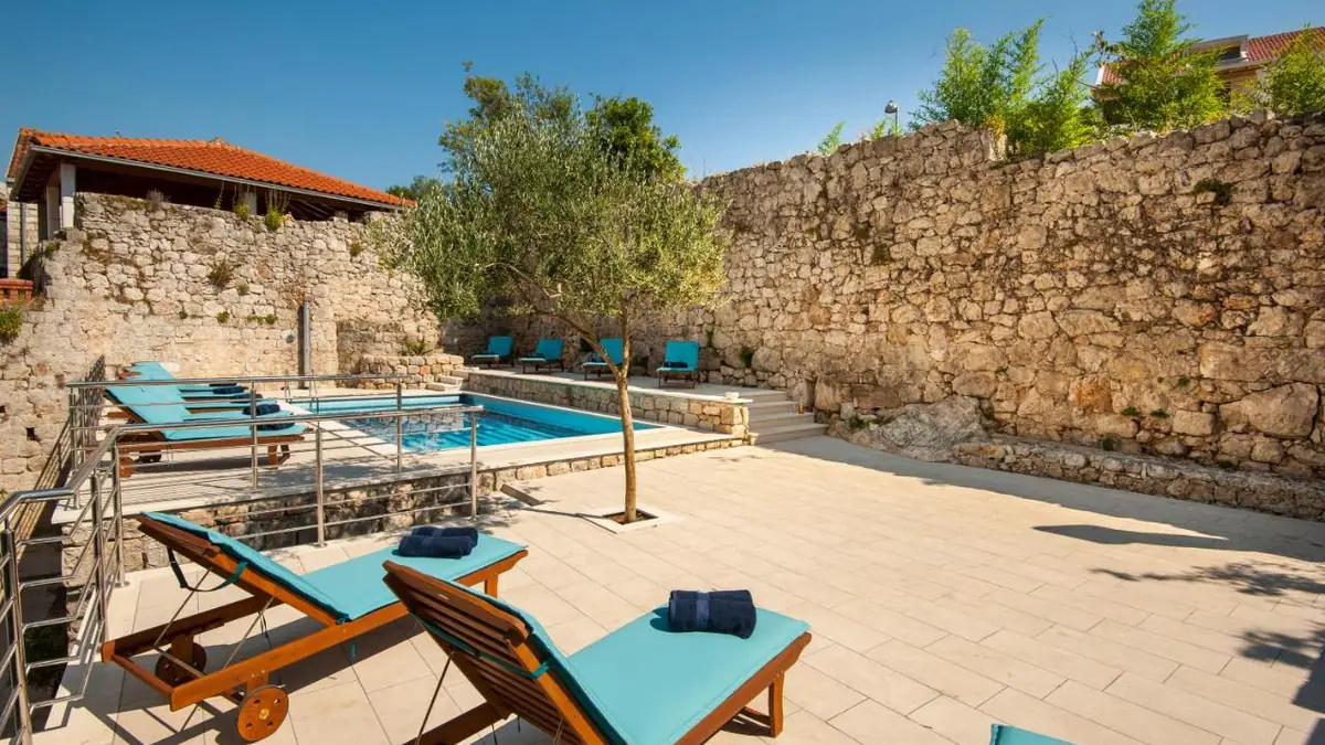 Outdoor pool at California Apartments with turquoise sun loungers and a stone wall